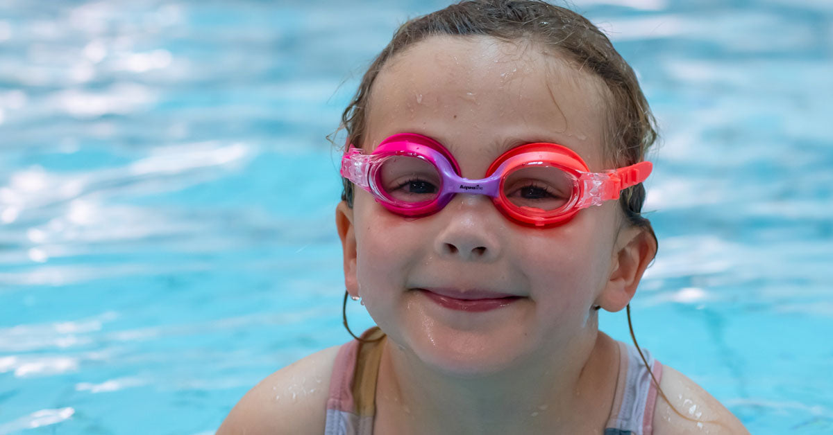 A smiling kid wearing a colourful pink and purple goggles from Aqualine Swim in New Zealand.