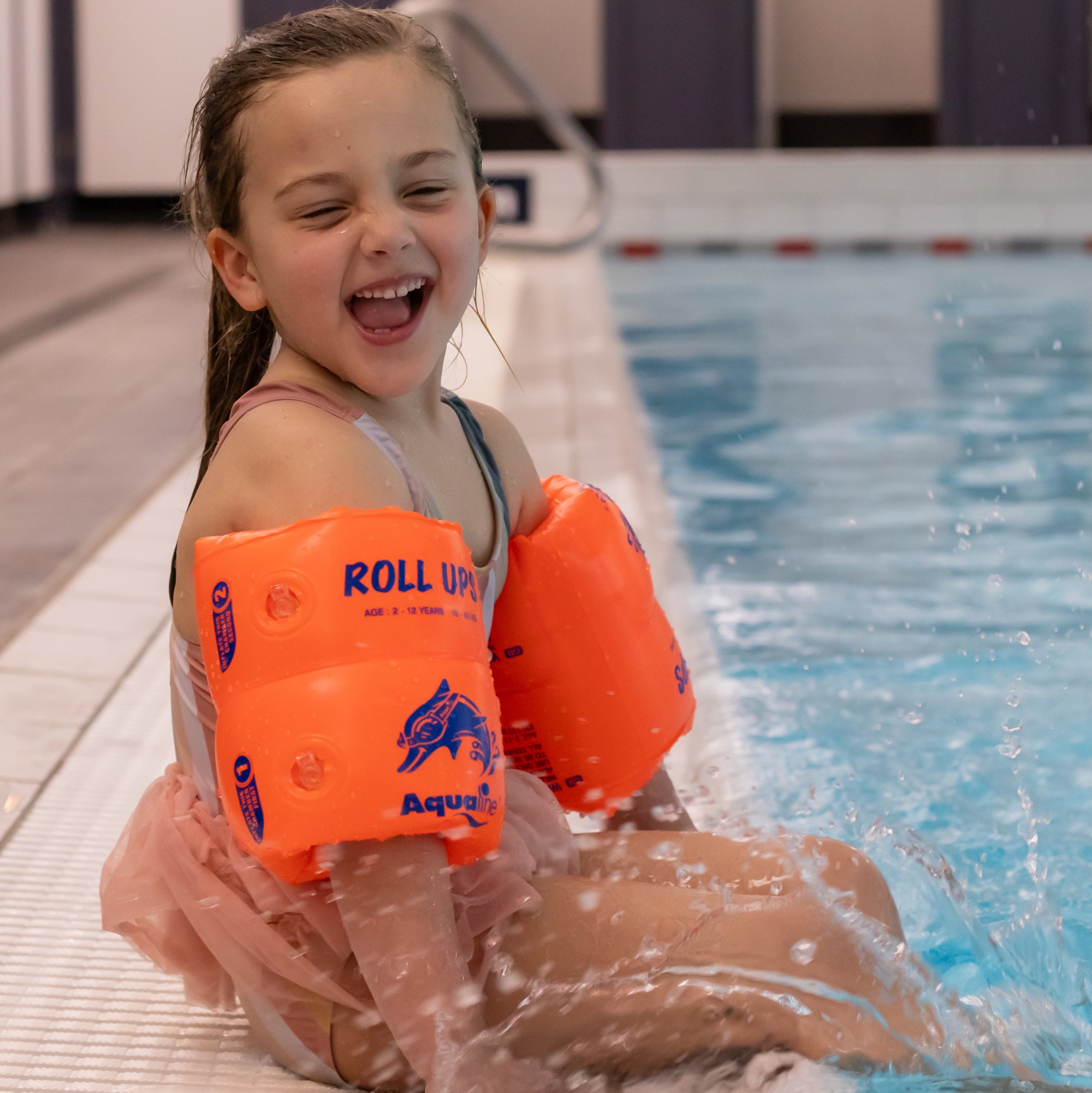 Child wearing orange 'Roll Up' swimming arm bands on pool edge