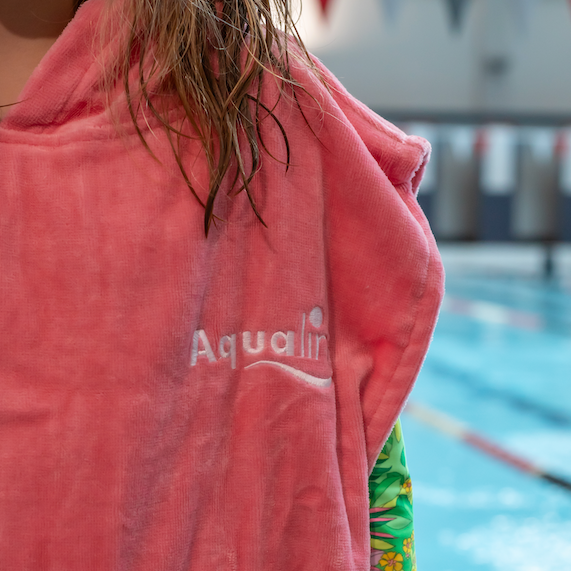 Person wearing a pink 'Aqualine' towel by a pool
