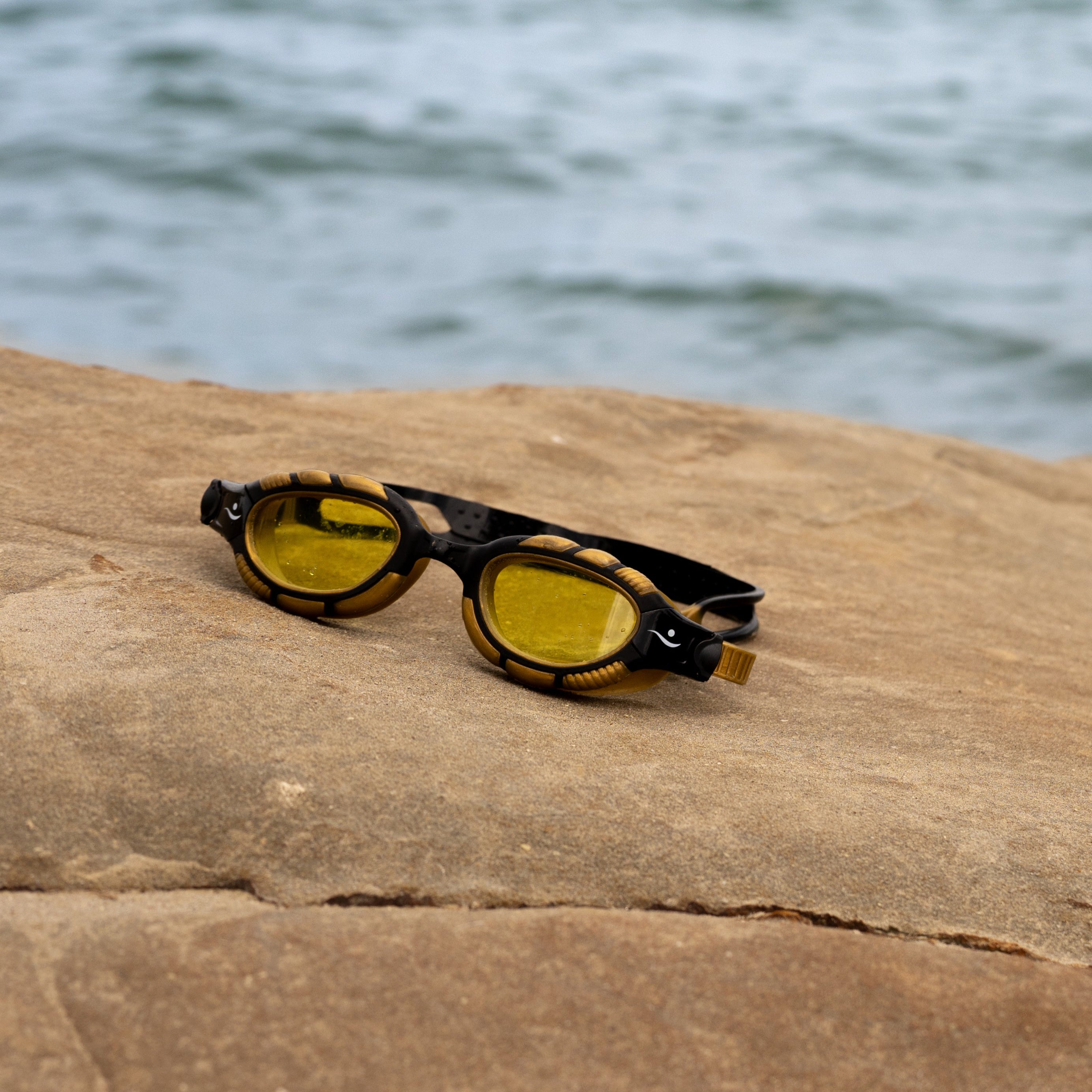 Yellow swim goggles on a rock with water in the background